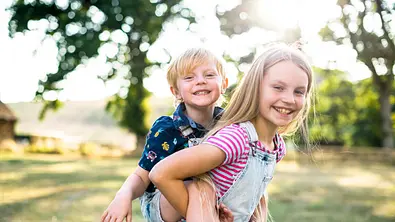 Eine große Schwester trägt stolz ihren kleinen Bruder auf ihrem Rücken. - Foto: Rawpixel/iStock