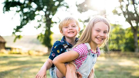 Eine große Schwester trägt stolz ihren kleinen Bruder auf ihrem Rücken. - Foto: Rawpixel/iStock