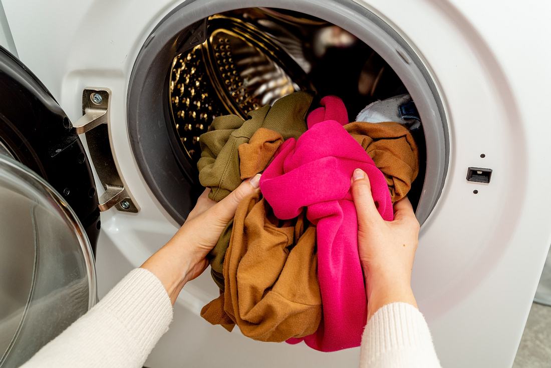 Person, die bunte Kleidung in die Trommel einer Waschmaschine legt, Vorderansicht. Waschen schmutziger Kleidung in der Waschmaschine.