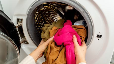 Person, die bunte Kleidung in die Trommel einer Waschmaschine legt, Vorderansicht. Waschen schmutziger Kleidung in der Waschmaschine. - Foto: Damian Lugowski/iStock