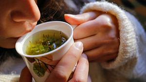 Eine Frau auf der Couch mit Heilkräutertee an der Hand - Foto: eyyazalacam/iStock