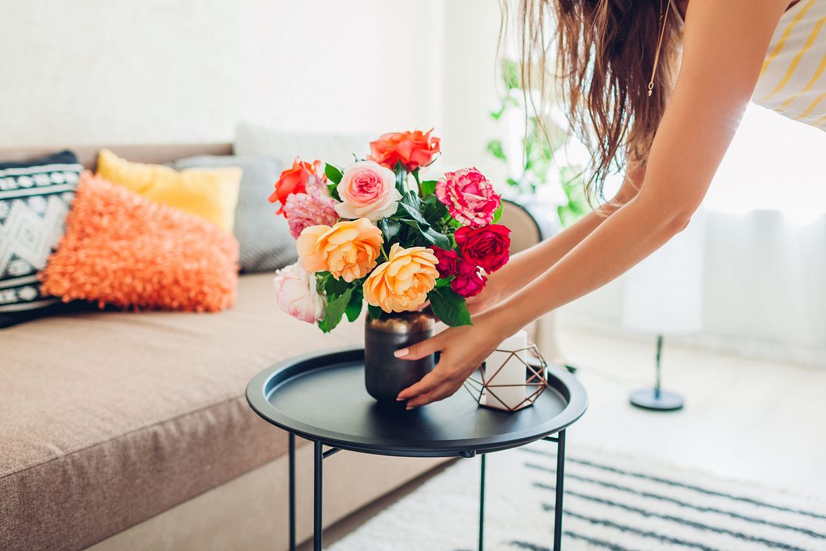 Frau legt Vase mit Blumen Rosen auf Tisch und sorgt für Gemütlichkeit in Wohnung.