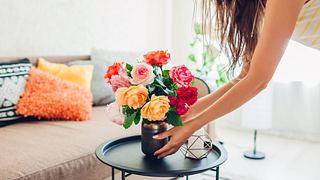 Frau legt Vase mit Blumen Rosen auf Tisch und sorgt für Gemütlichkeit in Wohnung. - Foto: Maryviolet/iStock
