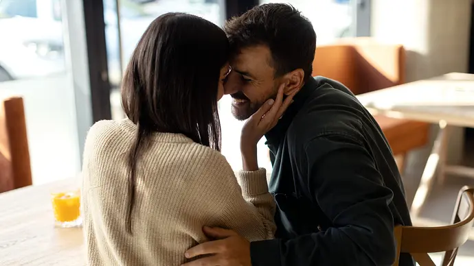 Junges heterosexuelles Paar umarmt sich sitzend in einem Café. - Foto: momcilog/iStock