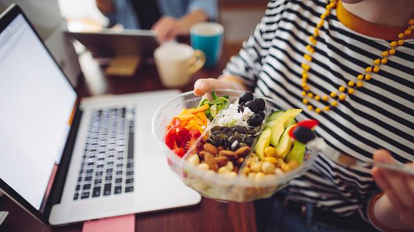 Person sitzt beim Essen zu Hause am Laptop.  - Foto: Eva-Katalin/iStock