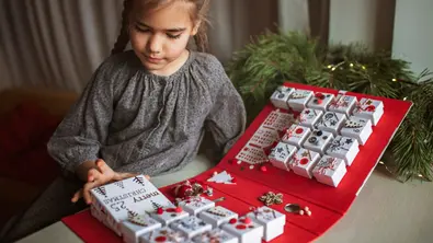 Ein kleines Mädchen betrachtet einen Adventskalender. - Foto: iStock/Maria Symchych-Navrotska