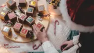 Eine Frau mit Weihnachtsmütze füllt einen Adventskalender - Foto: iStock/NataKor