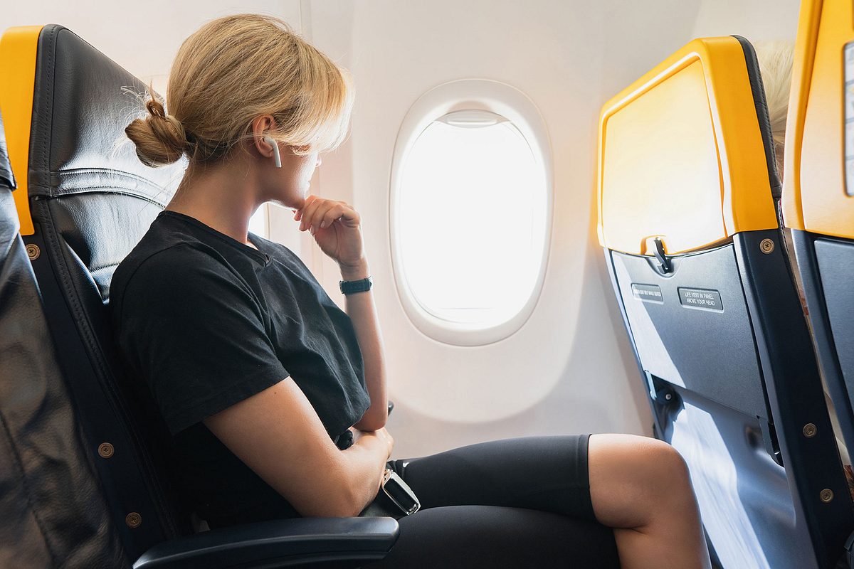 Frau sitzt im Flugzeug und schaut aus dem Fenster.