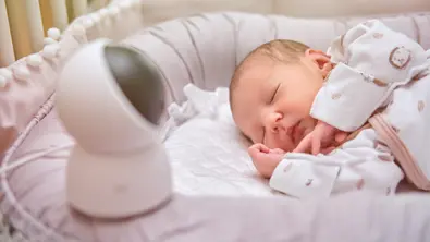 Neugeborenes liegt im Bett und schläft daneben steht eine Überwachungskamere - Foto: iStock/Andrey Zhuravlev