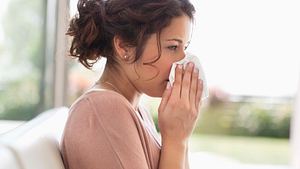 Frau zu Hause, putzt sich die Nase vor offenem Fenster - Foto: Paul Bradbury / iStock