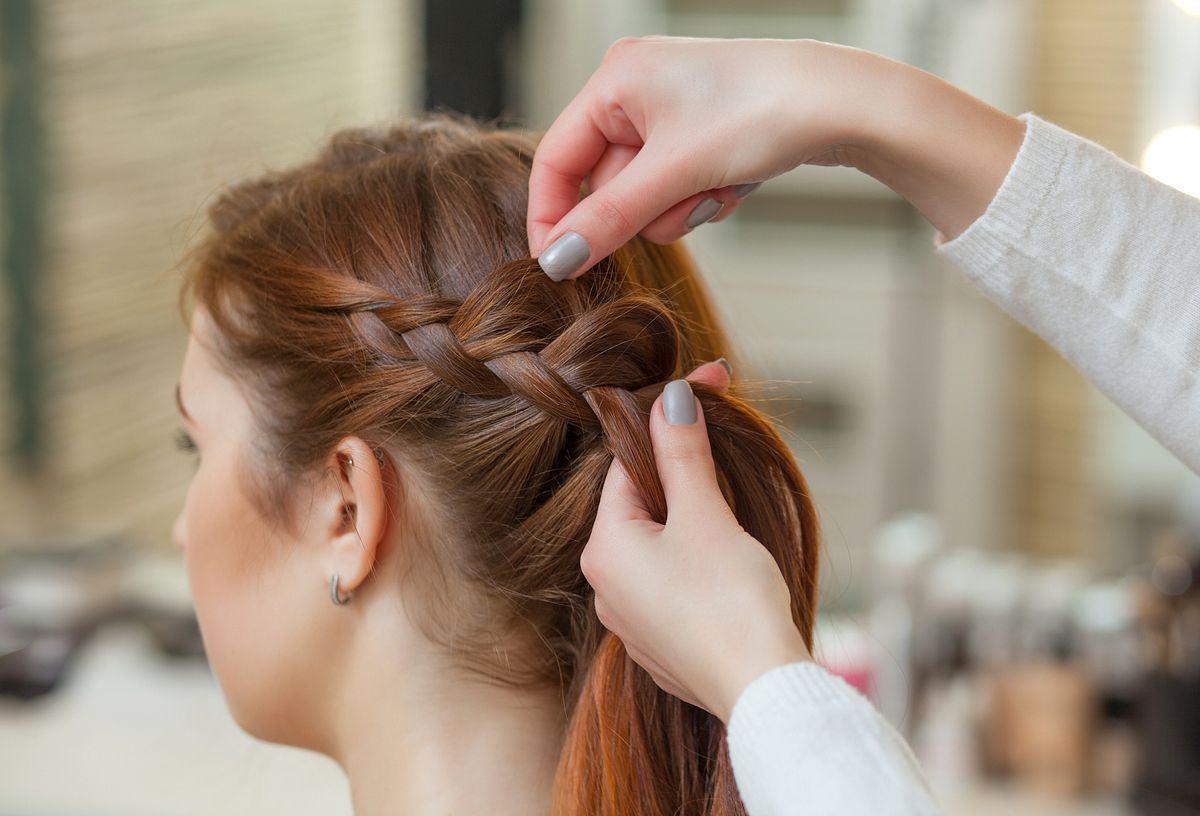 Frau mit rötlichem Haar bekommt seitlichen Zopf gelfochten.