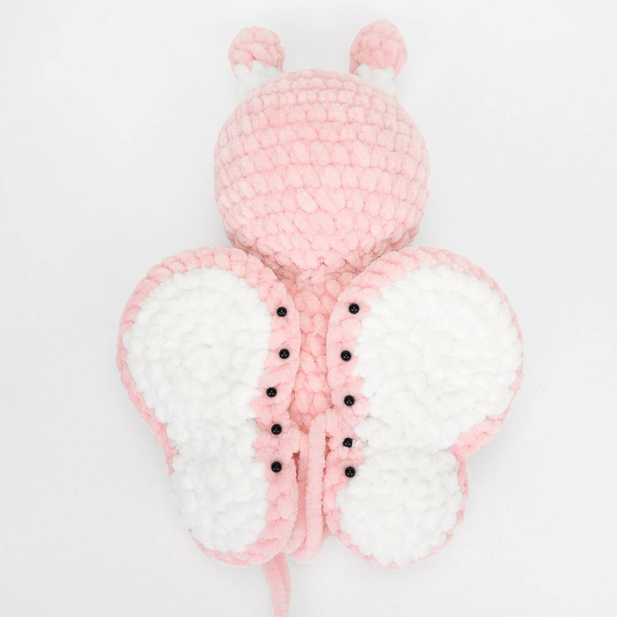 Anleitung Schmetterling häkeln Stepfoto 5 Die Flügel eines gehäkelten rosa-weißfarbenen Plüsch-Schmetterlings anbringen.