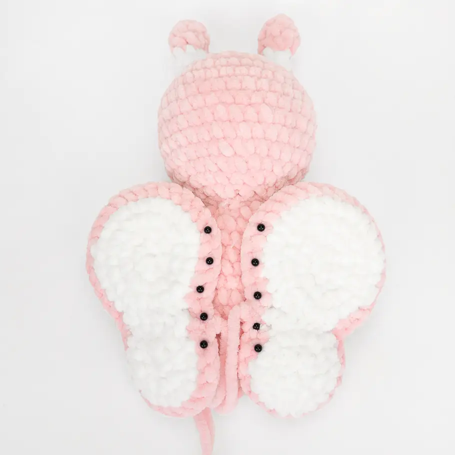 Die Flügel eines gehäkelten rosa-weißfarbenen Plüsch-Schmetterlings anbringen.