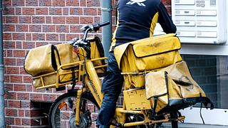 Unerkennbarer Postbote stellt Pakete und Briefe per Fahrrad zu. - Foto: IMAGO / Michael Gstettenbauer
