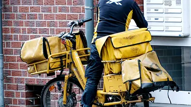 Unerkennbarer Postbote stellt Pakete und Briefe per Fahrrad zu. - Foto: IMAGO / Michael Gstettenbauer