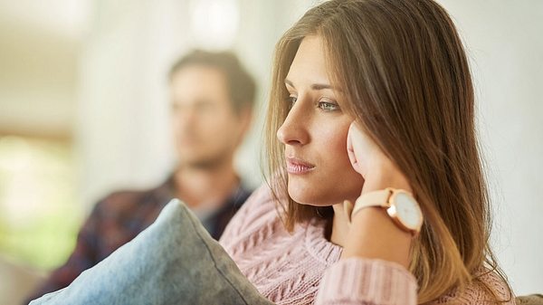 Junge Frau sieht traurig aus, ihr Freund sitzt im Hintergrund - Foto: PeopleImages / iStock