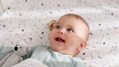 Baby liegt auf einer Decke und lächelt. - Foto: iStock/Liudmila Chernetska