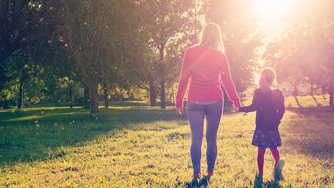 Frau geht mit Kind an der Hand im Sonnenlicht über eine Wiese (Themenbild) - Foto: IvanJekic/iStock