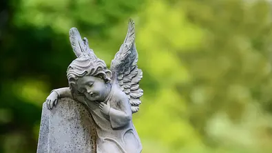 Kinderengelstatue auf Grabstein. Statue ruht auf kleinem Grabstein. - Foto: Sitikka / iStock