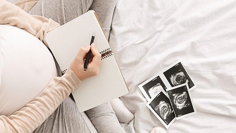 Schwangere Frau gestaltet Babybuch - Foto: iStock/Prostock-Studio