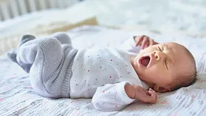 Vollaufnahme von einem Baby, dass auf dem Bett liegt und ausgiebig gähnt - Foto: iStock/encrier