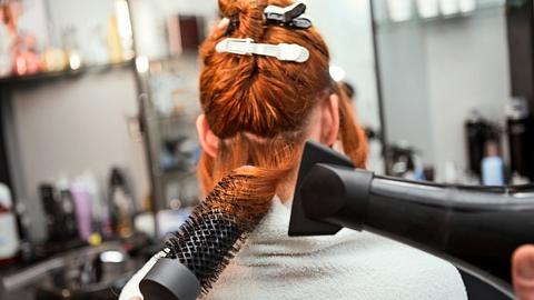 Das Haar einer rothaarigen Frau wird mit einer Rundbürste geföhnt. - Foto: Nastasic/iStock (Themenbild)