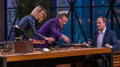 Janna Ensthaler und Ralf Dümmel beugen sich über den Tisch, Nils Dethloff sitzt. - Foto: RTL / Bernd-Michael Maurer