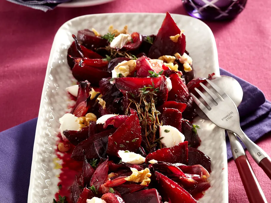 Auf einem gedeckten Tisch steht eine weiße Porzellanplatte mit Rote Bete Salat, Ziegenkäse und Walnüssen