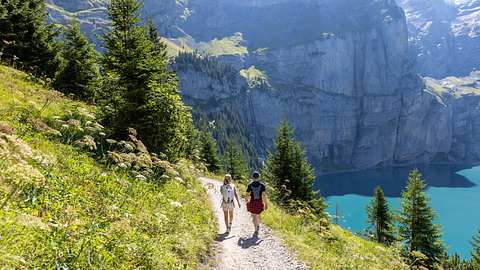 Zwei Personen wandern im Sommer in einer wunderschönen Alpenlandschaft in den Schweizer Alpen und genießen die Natur. - Foto: Mystockimages/iStock