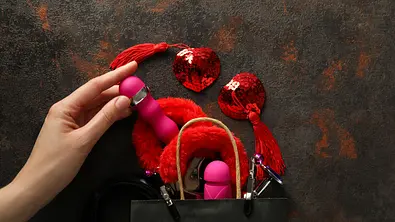 Eine schwarze Papiertüte mit verschiedenen Sex-Toys. Eine weibliche Hand nimmt ein Spielzeug heraus. - Foto: Artico/iStock