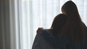 Zwei Frauen stehen Arm in Arm am Fenster und blicken nach draußen. - Foto: iStock/Farknot_Architect