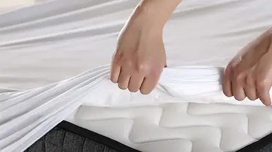 Hand einer Frau bezieht ein Bett mit einem Spannbettlaken - Foto: iStock/stockar