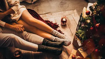 Vogelperspektive: Ein heterosexuelles Paar, dessen Köpfe man nicht sieht, sitzt entspannt auf einer Decke vor dem Weihnachtsbaum. - Foto: wundervisuals/iStock