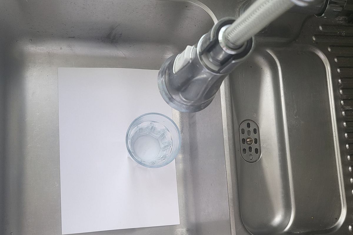 Ein Blatt Papier, darauf ein Glas Wasser im Küchen-Spülbecken 