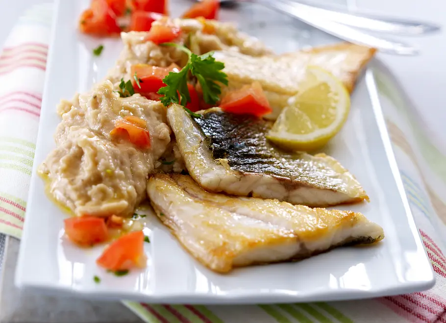 Bohnen-Püree zu gebratenem Wolfsbarsch und Tomatensalat Bohnen-Püree zu drei gebratenem Wolfsbarschfilets, garniert mit Tomatenwürfeln, Petersilie und einem Zitronenviertel.