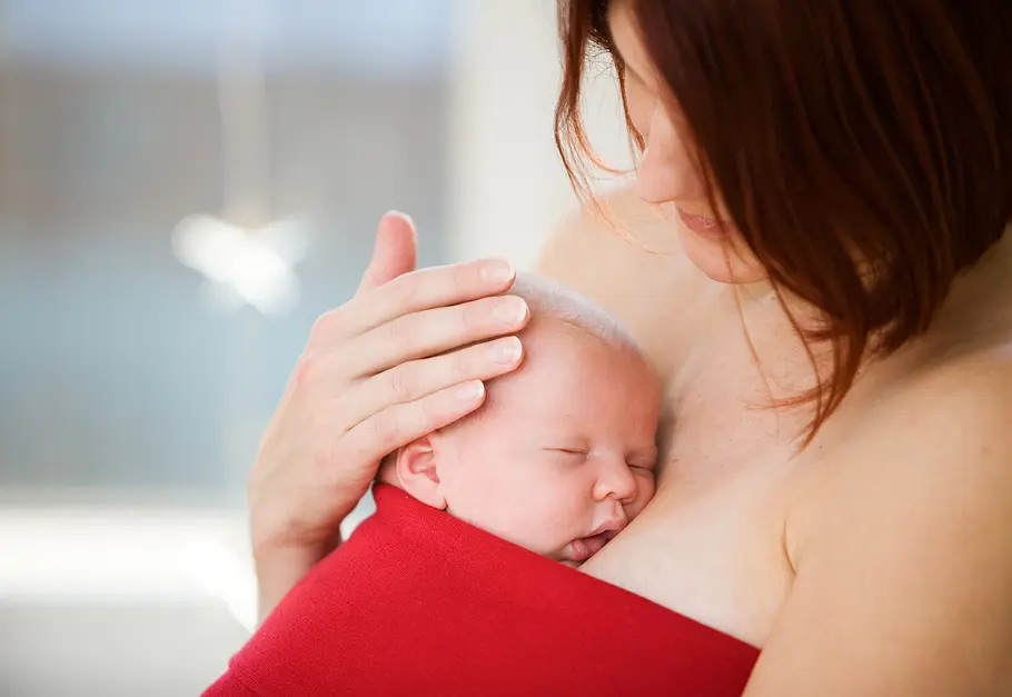 Bonding-Top Mutter hält ihr Neugeborenes auf ihrer nackten Brust unter einem Bonding-Top in den Armen