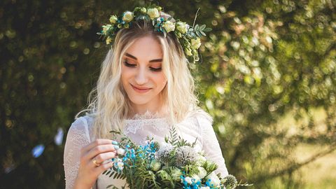 Eine Braut trägt passend zu ihrem Brautstrauß eine Hochzeitsfrisur mit Blumenkranz. - Foto: Roman Chekhovskoy/iStock