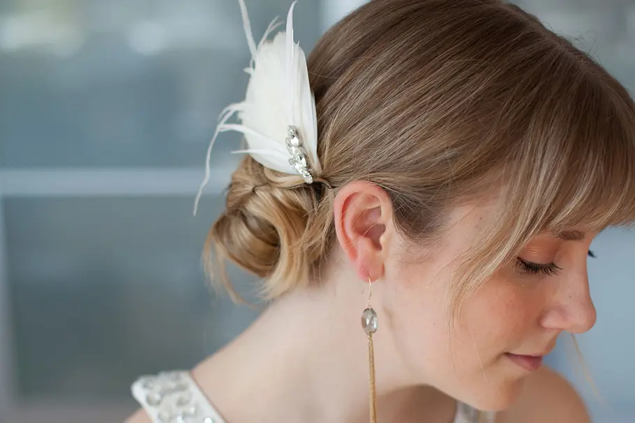 Braut trägt zu ihrem tiefen Dutt ein Haar-Accessoire mit Federn. Braut trägt zu ihrem tiefen Dutt ein Haar-Accessoire mit Federn.