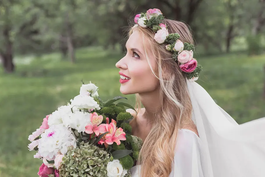 Sanfte Wellen in Kombination mit einem Blumenkranz (passend zum Brautstrauß) schmeicheln herzförmigen Gesichtszügen. Braut trägt sanfte Wellen mit einem Blumenkranz passend zu ihrem Brautstrauß.