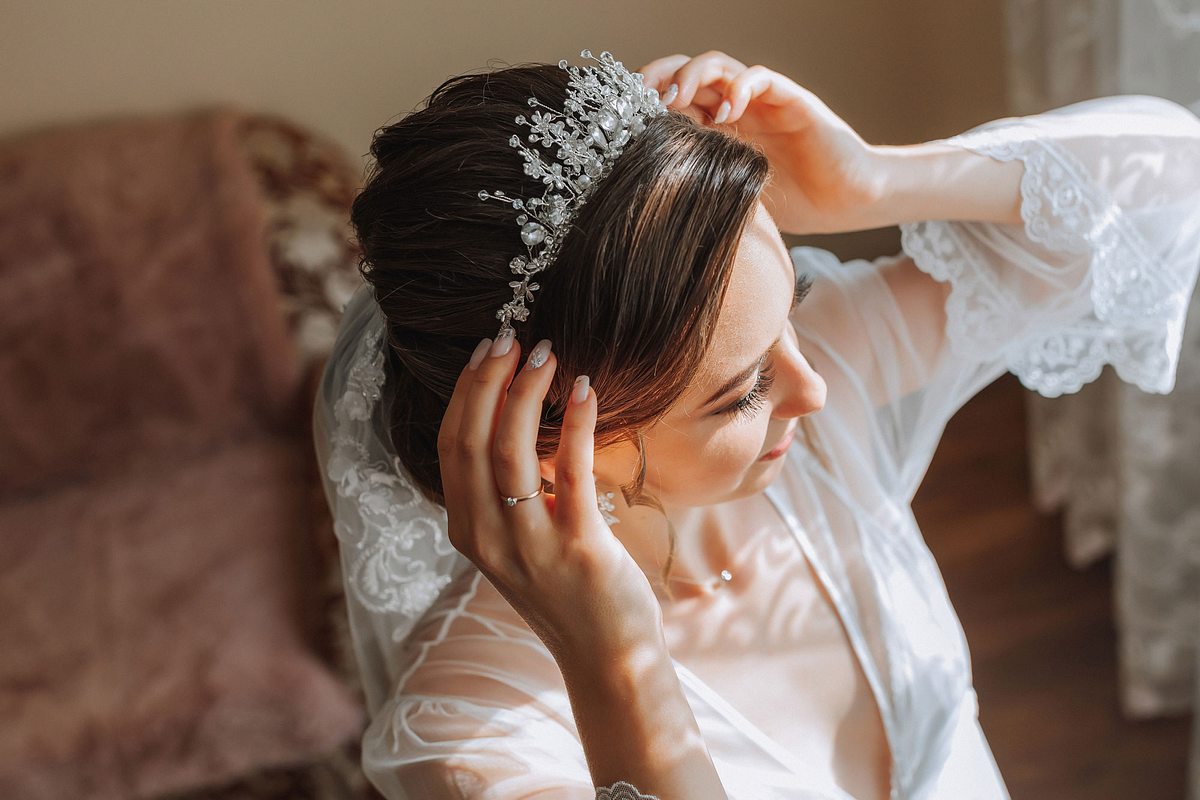 Braut mit Hochsteckfrisur setzt sich ein Diadem auf. 