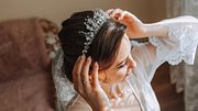 Braut mit Hochsteckfrisur setzt sich ein Diadem auf.  - Foto: Docinets Vasil/iStock 