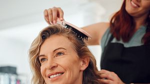 Frau mit blondem Haar bekommt die Haare gebürstet. - Foto: PeopleImages/iStock (Themenbild)
