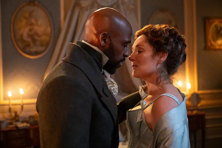 Lord Anderson und Lady Violet Bridgerton in historischer Kleidung stehen sich in einem stimmungsvoll beleuchteten, eleganten Raum sehr nahe gegenüber und bereiten sich auf einen intimen Moment vor. Im Hintergrund brennen Kerzen und an der Wand hängen Gemälde.