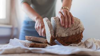 Nahaufnahme einer weiblichen Hand, die ein Messer nimmt und hausgemachten Laib Brot schneidet - Foto: Dobrila Vignjevic/iStock