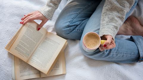 Frau die ein Buch liest im Bett mit Kaffee - Foto: Getty Images / Jamie Grill