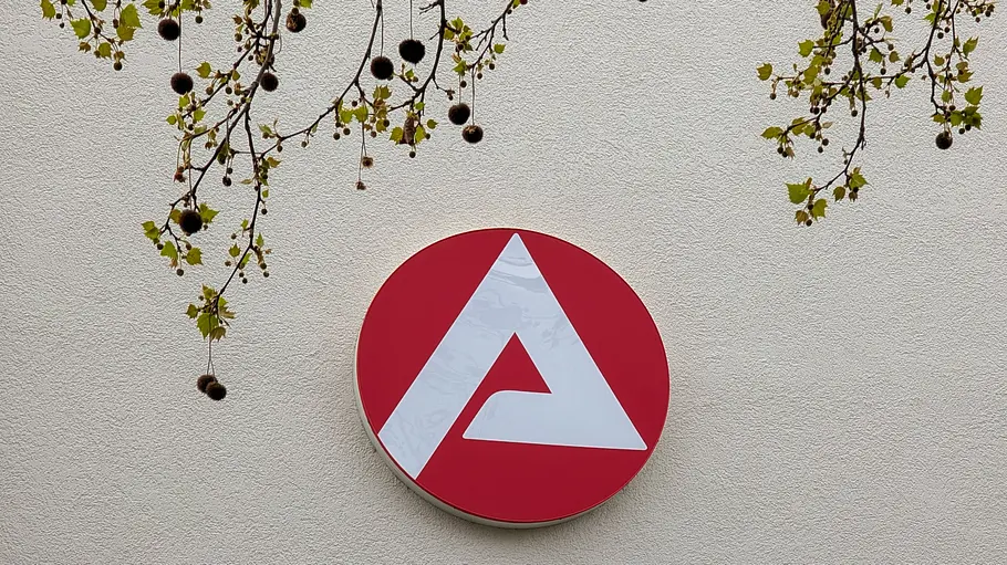 Agentur für Arbeit Logo der Bundesagentur für Arbeit an einer Außenwand, darüber Äste mit Blättern.