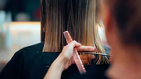 Eine Frau mit dunklem Haar, die mit dem Rücken zur Kamera sitzt, lässt sich ihr Haar schneiden. - Foto: nicoletaionescu/iStock (Themenbild) Eine Frau mit dunklem Haar, die mit dem Rücken zur Kamera sitzt, lässt sich ihr Haar schneiden. - Foto: nicoletaionescu/iStock (Themenbild)