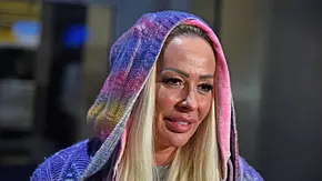 Cora Schumacher trägt eine bunte Strickjacke. Die Kapuze hat sie über den Kopf gezogen. Sie trägt die blonden Haare offen. - Foto: IMAGO / Gartner Cora Schumacher trägt eine bunte Strickjacke. Die Kapuze hat sie über den Kopf gezogen. Sie trägt die blonden Haare offen. - Foto: IMAGO / Gartner