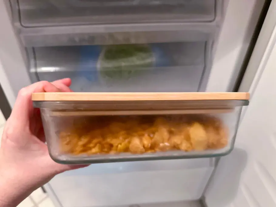 Tiefgekühlte Cornflakes Eine Hand hält eine verschlossene Glasschale mit tiefgekühlten Cornflakes und im Hintergrund ist der Gefrierschrank zu sehen.