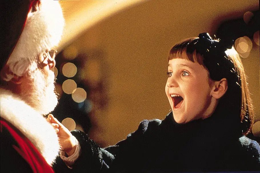 Das Wunder von Manhattan Der Weihnachtsmann hat ein kleines Mädchen auf dem Arm. Sie freut sich total und hat den Mund weit offen.